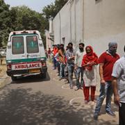 En ambulans med en covidpatient lämnar ett sjukhus samtidigt som människor köar för att coronatesta sig vid ett sjukhus i New Delhi