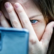 En kvinna tittar på sin mobil med handen för ansiktet. Illustrationsbild. 