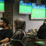 Människor följer en fotbollsmatch från ett café i Teheran.