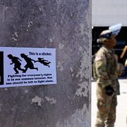 Ett klistermärke som kritiserar migrationspolisen syns på en vägg bredvid agenter från departementet för inrikes säkerhet och medlemmar av nationalgardet.