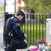 Poliser vid en minnesplats där människor lämnat blommor och ljus efter trippelmordet. 