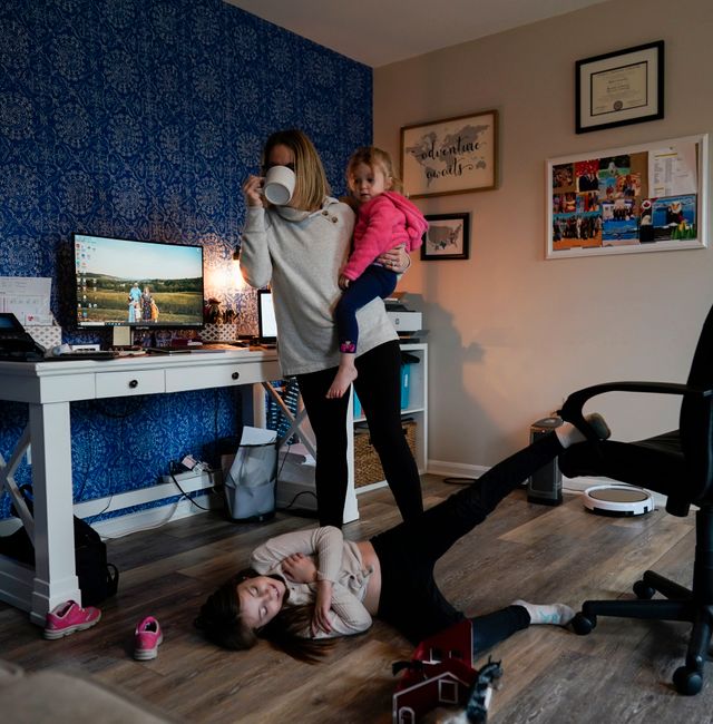 Tara Carpenter holds Alyssa Carpenter, 2, as Hailey Carpenter, 9, plays at her feet and Audrey Carpenter, 5, sits left, as she ties to work in her home office in Haymarket, Va., Friday, Jan. 28, 2022. Alyssa has had COVID-19 twice and suffers long-term symptoms. All three girls are part of a NIH-funded multi-year study at Children's National Hospital to look at impacts of COVID-19 on children's physical health and quality of life. Carolyn Kaster / AP