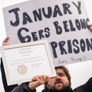 En demonstrant vid Kapitolium får sitt plakat blockerat av ett benådningscertifikat vid protster under femårsdagen för stormningen.