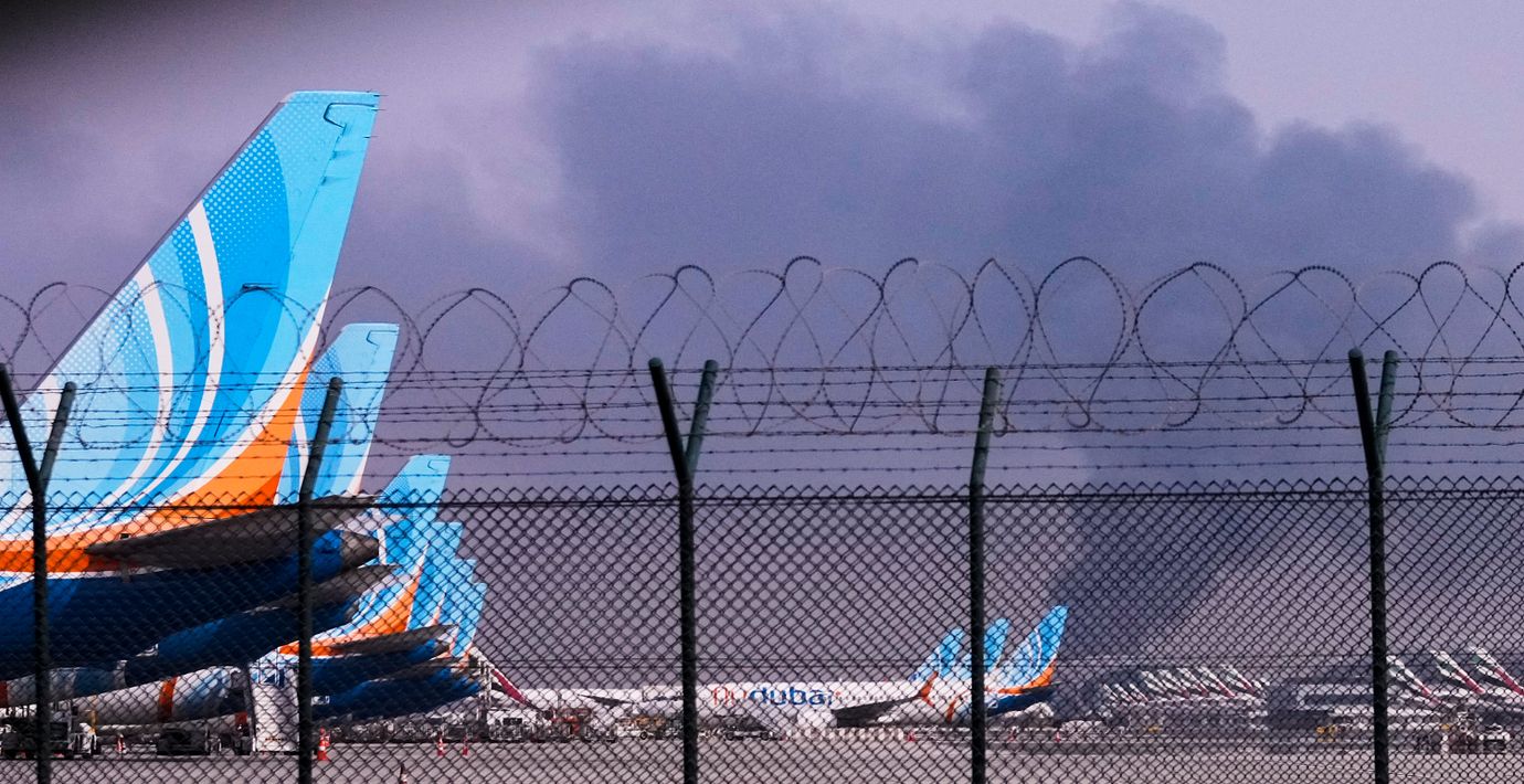 Rökmoln från en drönarattack stiger bakom flygplan parkerade på Dubais internationella flygplats. 