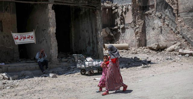 Irakiska flickor går vid en förstörd byggnad i västra Mosul, Irak. På skylten står det ”Familjer finns här”.  SAFIN HAMED / AFP