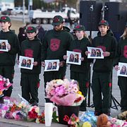 Människor håller upp bilder på offren vid brottsplatsen förra veckan.