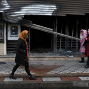 Shariar-invånare går förbi en bank som skadades i protesterna. 