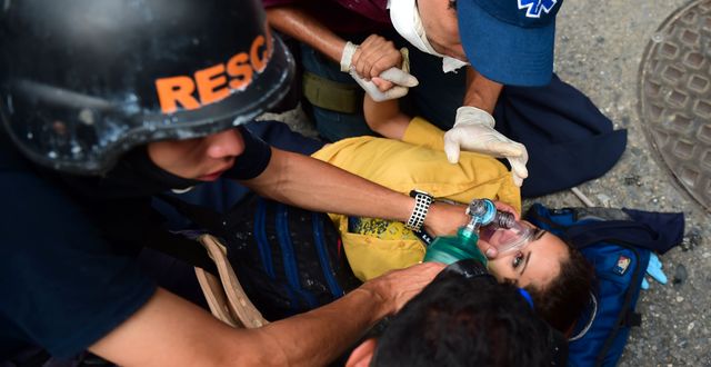En kvinnlig demonstrant får vård efter att ha skadats i sammandrabbningar med polis i Venezuelas huvudstad Caracas i går. RONALDO SCHEMIDT / AFP