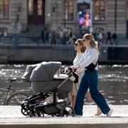 Människor med barnvagnar njuter i solen vid Nybrokajen i centrala Stockholm i april. 