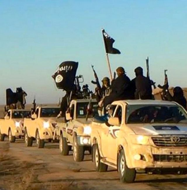 In this undated file photo released online in the summer of 2014 on a militant social media account, which has been verified and is consistent with other AP reporting, militants of the Islamic State group hold up their weapons and wave its flags on their vehicles in a convoy on a road leading to Iraq, in Raqqa, Syria. With Islamic State's near total defeat on the battle field, the extremist group has reverted to what it was before its spectacular series of conquests in 2014 a shadowy terror network that targets vulnerable civilian populations and exploits state weaknesses to incite on sectarian strife. AP