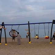 Människor gungar på en strand med Hormuzsundet i bakgrunden.