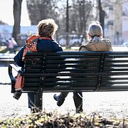 Två kvinnor njuter av vårsolen på en parkbänk på Karlaplan i Stockholm.