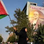 En iransk kvinna med en palestinsk fana inför en demonstration mot mordet på Hamasledaren Ismail Haniya framför en väggmålning av honom i Teheran, Iran, den 31 juli 2024.