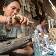 Indonesiska kvinnor som tillverkar hantverksprodukter att sälja på en turist-marknad på Bali. 