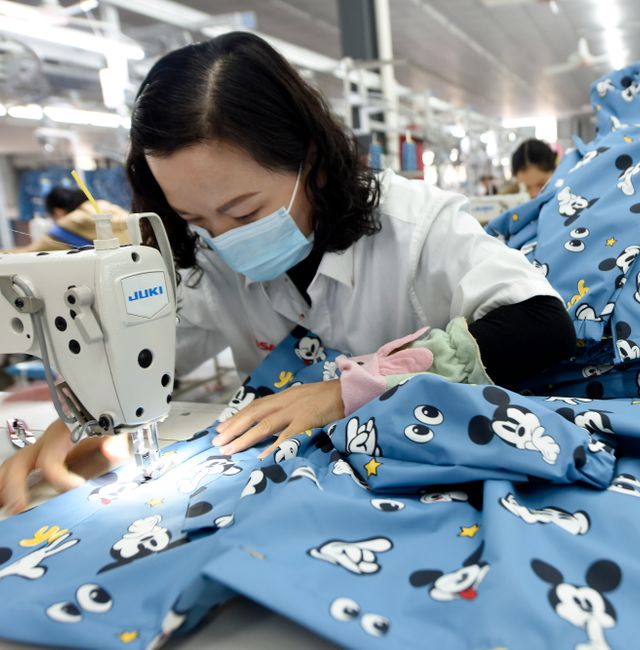 An employee wearing a face mask to protect herself against the coronavirus stitches clothing for export at a factory in Donghai county in eastern China's Jiangsu Province, Tuesday, Oct. 27, 2020. China's export growth accelerated in October, boosting the total so far this year back above pre-coronavirus levels for the first time. TT NYHETSBYRÅN