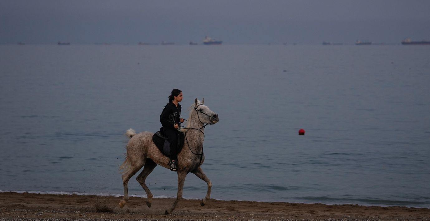 En ryttare rider längs stranden medan oljetankers och lastfartyg köar i Hormuzsundet utanför Khor Fakkan i Förenade Arabemiraten.