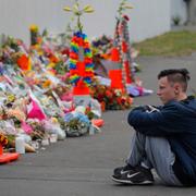 En student sitter vid havet av blommor vid attentatsplatsen i Christchurch. 