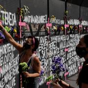 Kvinnor sätter fast blommor på ett staket i Mexico City, där namnen på mördade kvinnor skrivits.