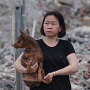 En kvinna med sin hund framför en byggnad som förstörts.