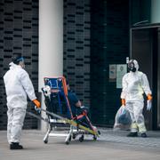 Personal iklädda skyddskläder hjälper en patient sittandes på en bår in på Karolinska sjukhuset i Solna.