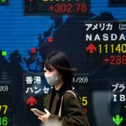 En kvinna går förbi en tavla i Tokyo som visar Nikkei och andra börsindex.