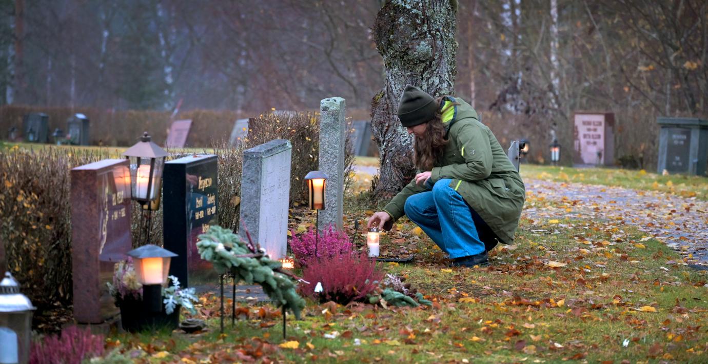  Arkivbild. Kvinna tänder ett ljus vid grav på kyrkogård. 
