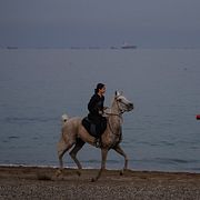 Oljetankers och fraktfartyg ligger på rad i Hormuzsundet utanför Khor Fakkan i Förenade arabemiraten, medan en ryttare rider längs stranden.