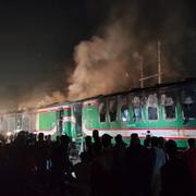 Människor ser på när ett passagerartåg brinner i Dhaka på fredagen. Minst fyra personer dog och flera skadades. Enligt polisen är branden ett sätt att skrämma människor inför helgens val i Bangladesh. 