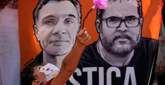 Ett barn leker med en blomma framför plakat med porträtt av journalisten Dom Phillips, till vänster, och urfolksexperten Bruno Pereira, till höger. Brasilia 19 juni. Eraldo Peres / AP
