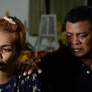 Mamman till barnet tröstas av hennes pappa i ett tempel i Phuket.