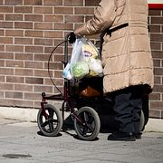 En pensionär med rullator går med matkassar längs en gångväg i Södertälje.