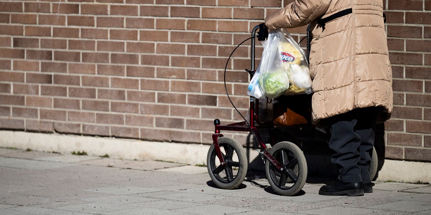 En pensionär med rullator går med matkassar längs en gångväg i Södertälje.