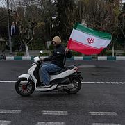 Man kör moped och håller upp en iransk flagga.