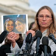 Annie Farmer håller upp en bild på sig själv och systern Maria på en pressträff i november.