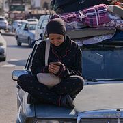 En kvinna sitter på en bil i södra Libanon och tittar på sin mobil.