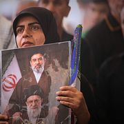 En irakisk kvinna deltar i sörjandet av ayatollan. Hon håller en bild av efterträdaren Mojtaba Khamenei, och hans avlidne far Ali Khamenei.
