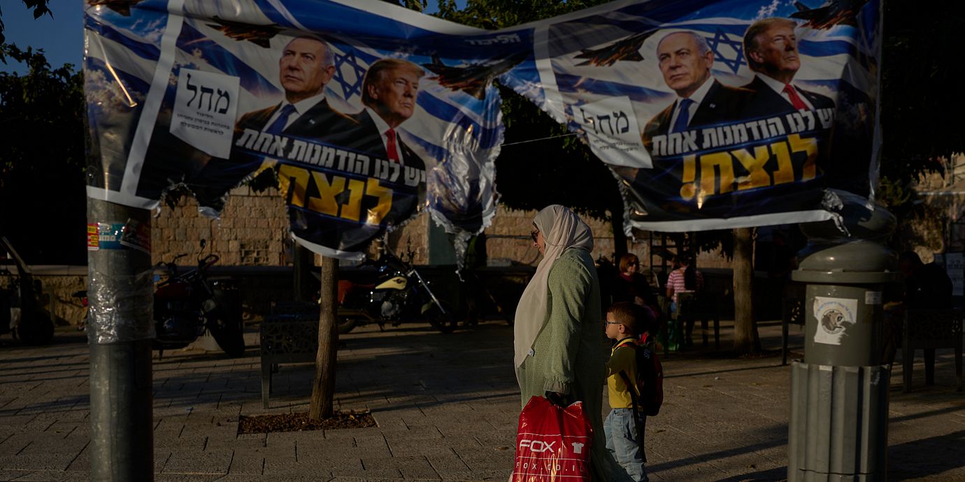 En kvinna och ett barn passerar en sönderriven valaffisch med Benjamin Netanyahu och Donald Trump i Jerusalem dagen efter det israeliska valet.
