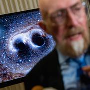 En visualisering av gravitationsvågor från två svarta hål visas bakom LIGO-grundaren Kip Thorne vid en presskonferens 2016, då forskare för första gången bekräftade Einsteins hundra år gamla teori.