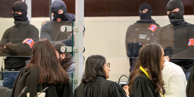 Maskerade poliser står bakom de tilltalade i en galsbur under rättegången. Olivier Matthys / AP