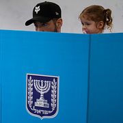 En man med ett barn i famnen förbereder sin valsedel i en vallokal i Tel Aviv.