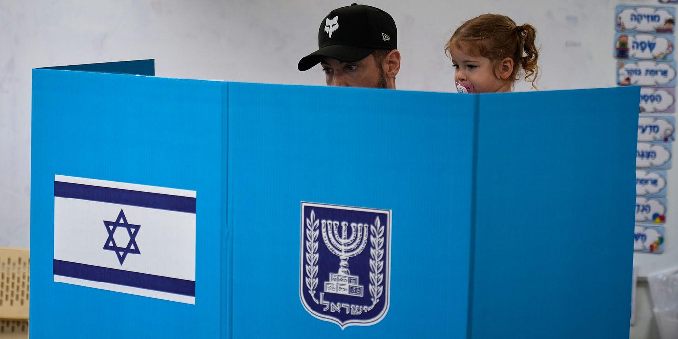 En man med ett barn i famnen förbereder sin valsedel i en vallokal i Tel Aviv.