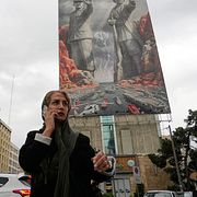 En kvinna pratar i telefon framför en propagandamålning som föreställer iranska nationalhjältar som blockerar Hormuzsundet. Bilden är tagen i mitten av april.