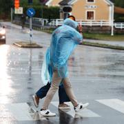 Ett par med regnponchos går snabbt över ett övergångsställe i regnet. 