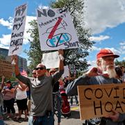 In this Aug. 30, 2020 file photo, Sal Lando, left, of Sterling, holds up signs during a protest against mandatory flu vaccinations, outside the Massachusetts State House, in Boston.