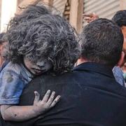 En man bär på ett barn som skadats i ett israeliskt flyganfall mot Gaza City.