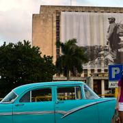 En kvinna poserar framför sin bil på revolutionstorget i Havana, framför en stor bild på Fidel Castro.