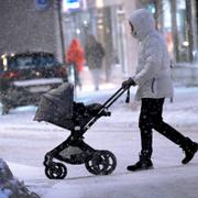 En person med barnvagn går över gatan i snöoväder. 