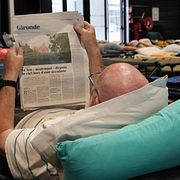 En evakuerad man i Bordeaux, som tvingades byta hängmattan mot britsen, läser tidningen om skogsbränderna.
