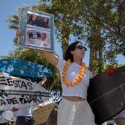 En demonstrant håller upp en skylt med foton på de tre utländska surfarna som hittats döda i Baja California.