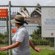 En kvinna vandrar förbi Operahuset i Sydney, som har spärrats av med stängsel.